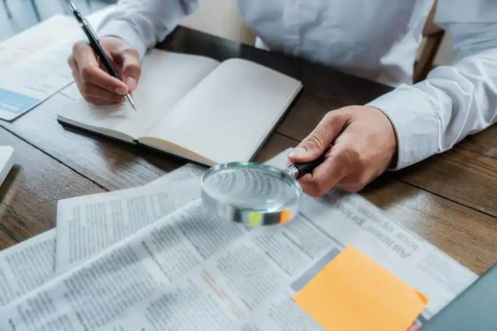 Midsection of businessman holding magnifying glass over newspaper 