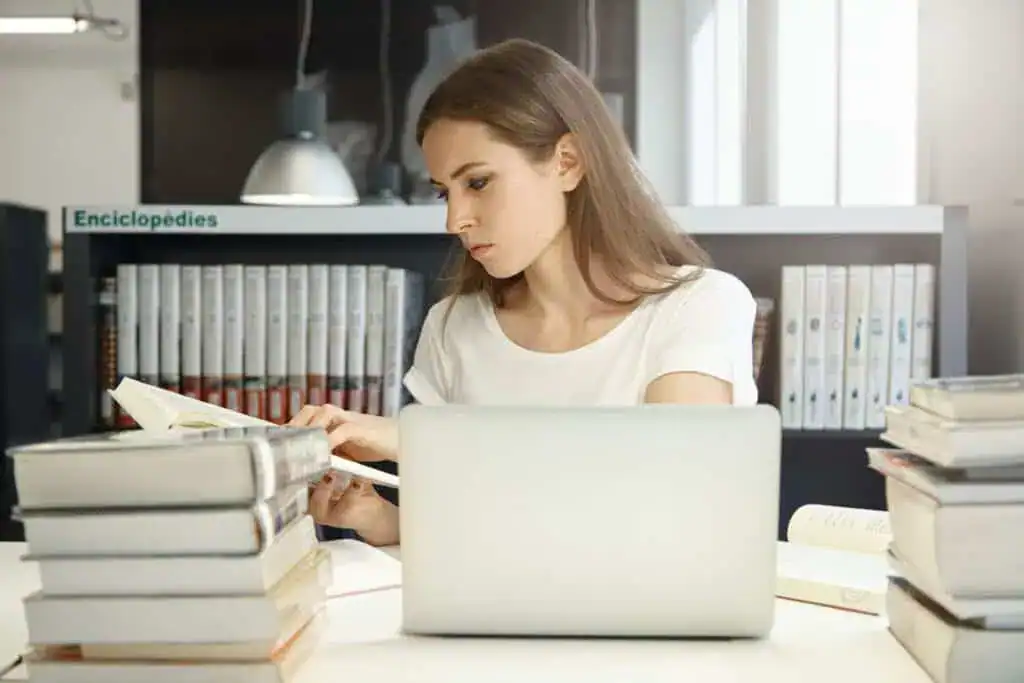 Woman studying with books and laptop in a library or study space.