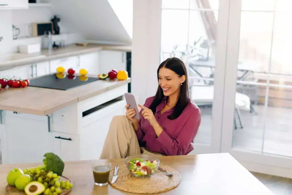 Happy woman using cellphone in kitchen 