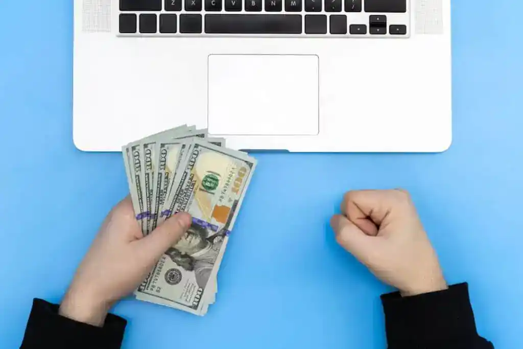 Como monetizar um blog: maneiras comprovadas de obter renda 5 Laptop e dinheiro nas mãos de um homem, vista superior